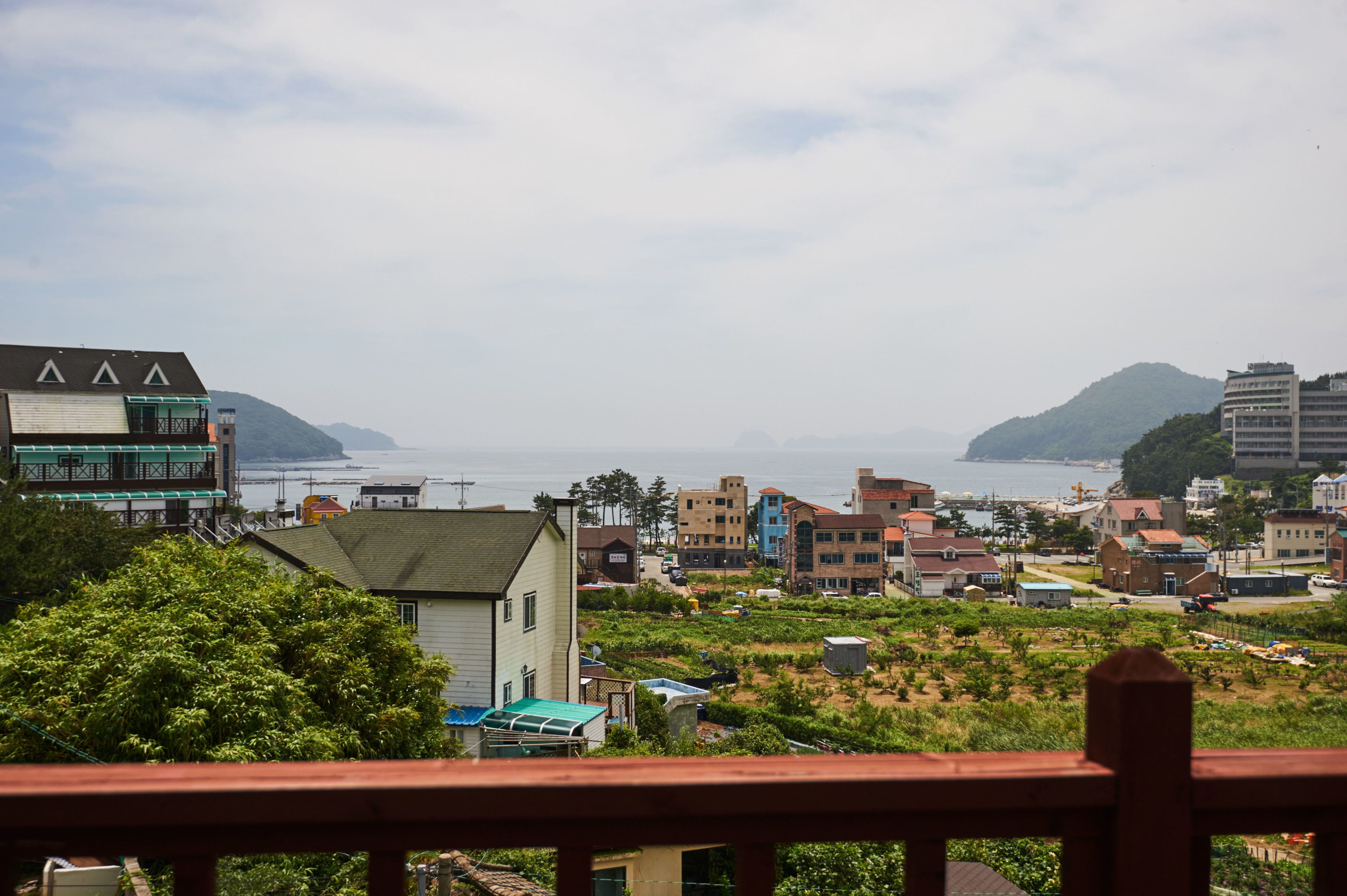 A coastal town with buildings, a view of the sea, and hills in the background.