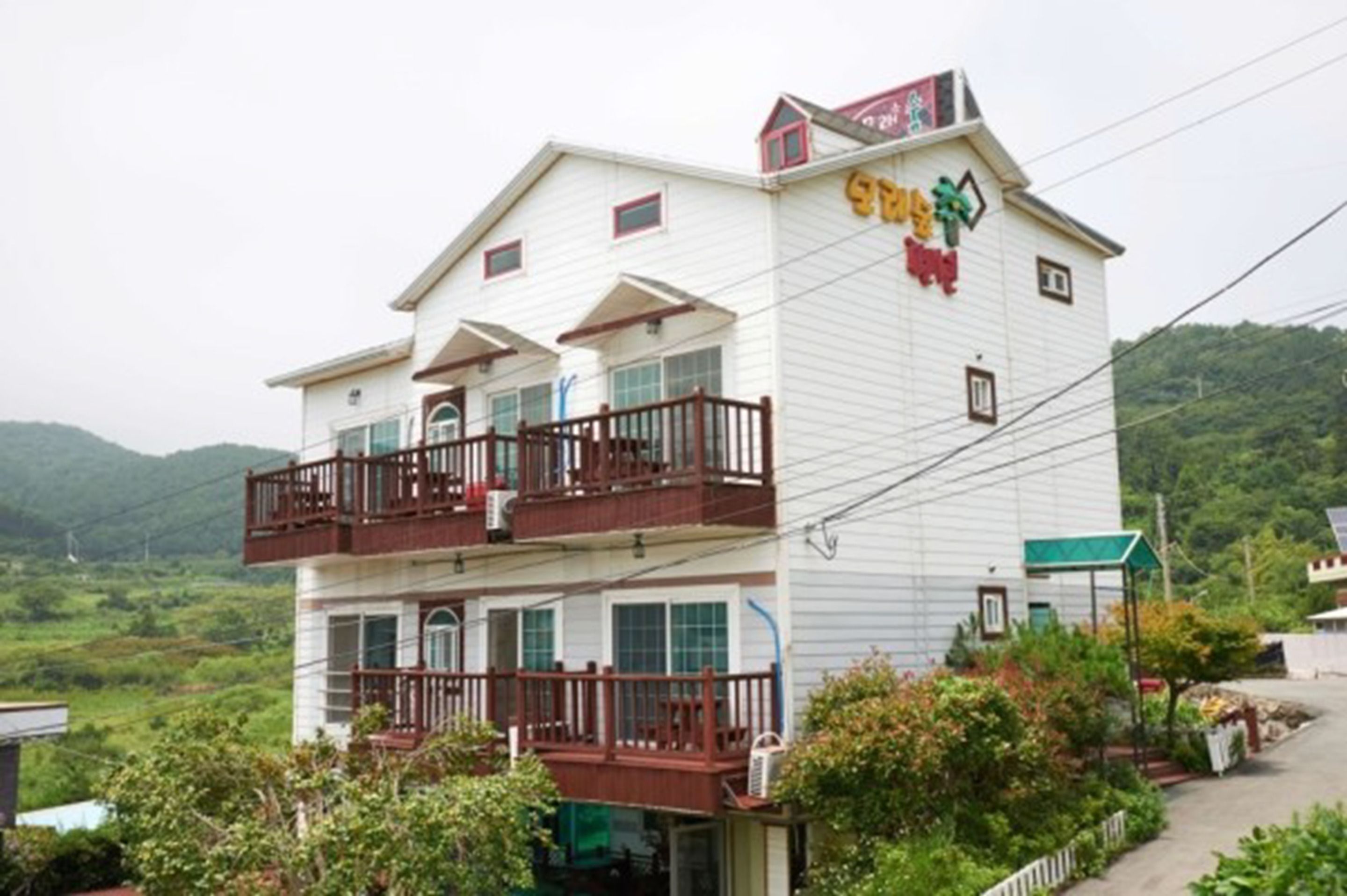 A two-story building with balconies, a sign with colorful characters, and a view of a green landscape.