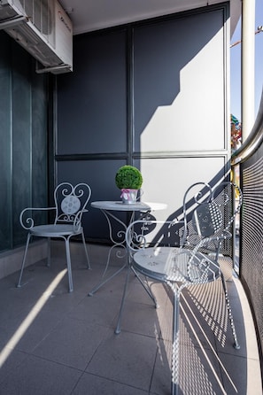 A balcony with metal chairs and a small table, a potted plant, and an air conditioning unit. - Apartment Eugen 2 (Novi Sad)