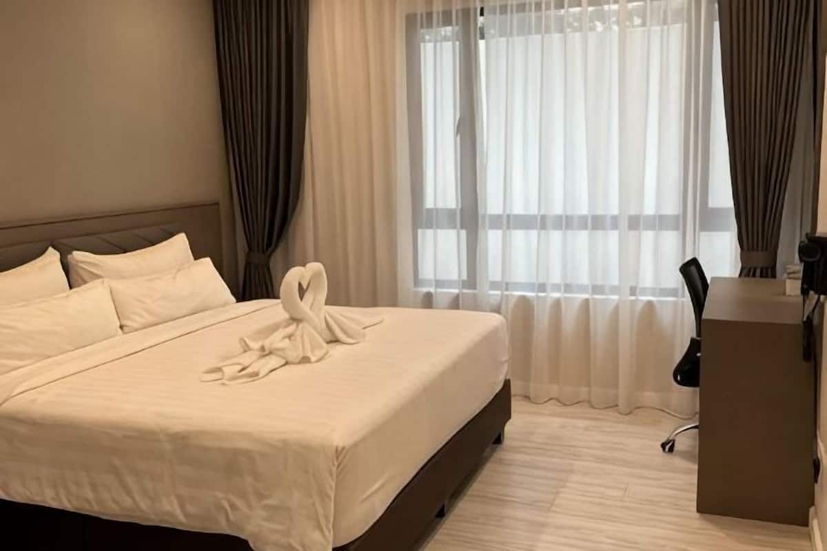 A hotel room with a large bed, a desk, and a window with curtains.