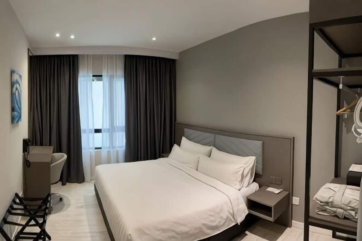 A modern hotel room with a large bed, a desk, a chair, and a wardrobe.