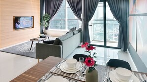 A modern dining area with a wooden table set for four, a TV mounted on the wall, and a large window with curtains. - Suasana Suites by Subhome (Johor Bahru)