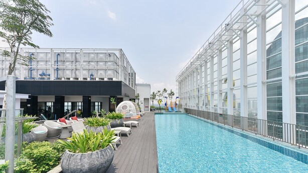 A modern pool area with lounge chairs and planters, surrounded by glass buildings. - Suasana Suites by Subhome (Johor Bahru)