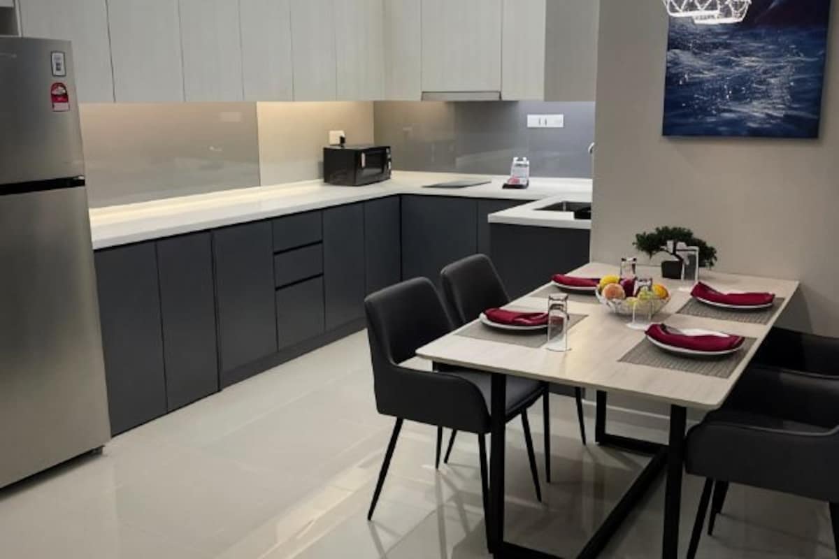 Una cocina moderna con armarios oscuros, un refrigerador de acero inoxidable y un comedor con una mesa dispuesta para dos.