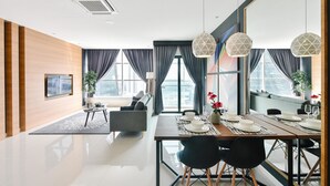 A modern dining area with a large table set for four, a sofa, and a city view through large windows. - Suasana Suites by Subhome (Johor Bahru)