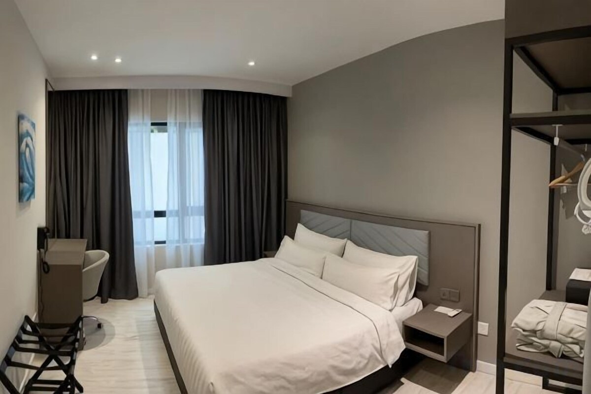 Moderni hotellihuone, jossa on suuri sänky, työpöytä ja vaatekaappi.