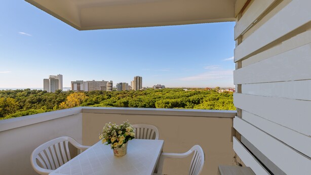 Varanda com mesa, cadeiras, um vaso de flores e vista para a cidade.