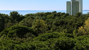 Um edifício alto com vista para o mar e vegetação densa em primeiro plano.