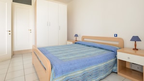 Quarto com cama, mesas de cabeceira, abajur e guarda-roupa.