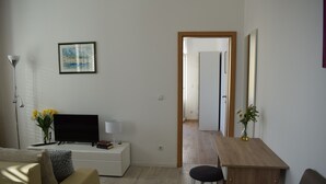 A modern living room with a flat-screen TV, a sofa, a coffee table, and a wooden desk with a chair. - Optimist Makarska Town Center (Makarska)