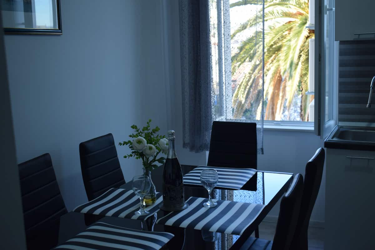 Un comedor con una mesa dispuesta para dos personas, manteles a rayas, un florero con flores y una botella.