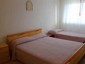 Une chambre avec deux lits simples, une table de chevet en bois, une petite table et un élément décoratif fixé au mur.