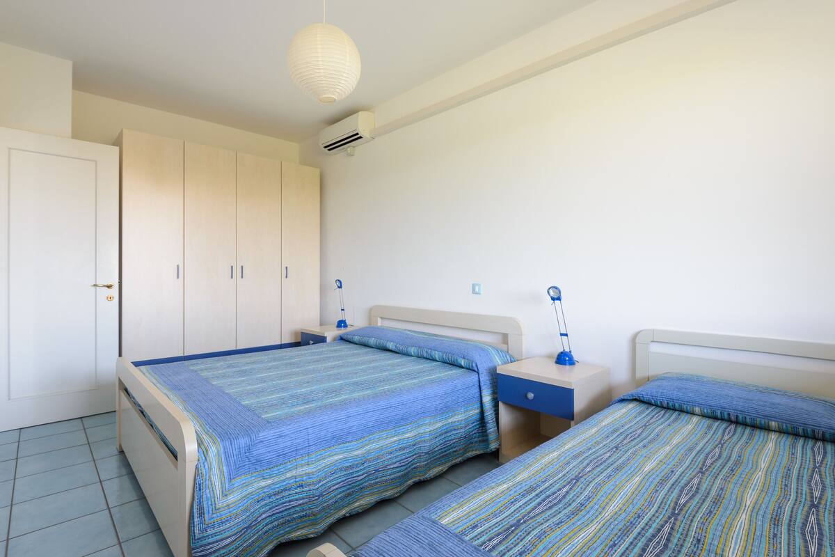 Une chambre avec deux lits, une armoire, une table de chevet avec une lampe et un appareil de climatisation.