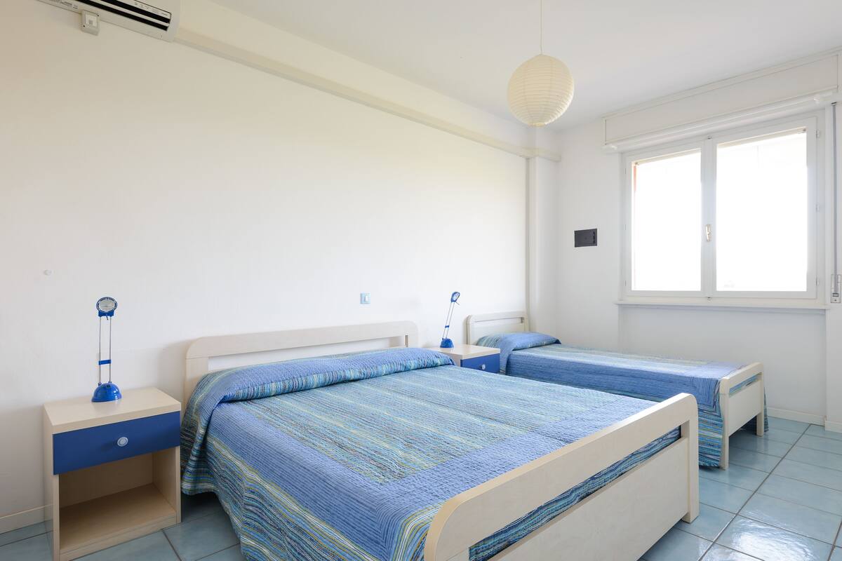 Une chambre avec deux lits simples, une table de chevet avec une lampe, une fenêtre et un ventilateur de plafond.