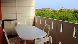 Ein Balkon mit einem weißen Tisch und Stühlen, im Hintergrund Grünflächen und Gebäude.