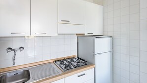 Eine Küche mit weißen Schränken, einer Spüle aus Edelstahl, einem Gasherd und einem weißen Kühlschrank.
