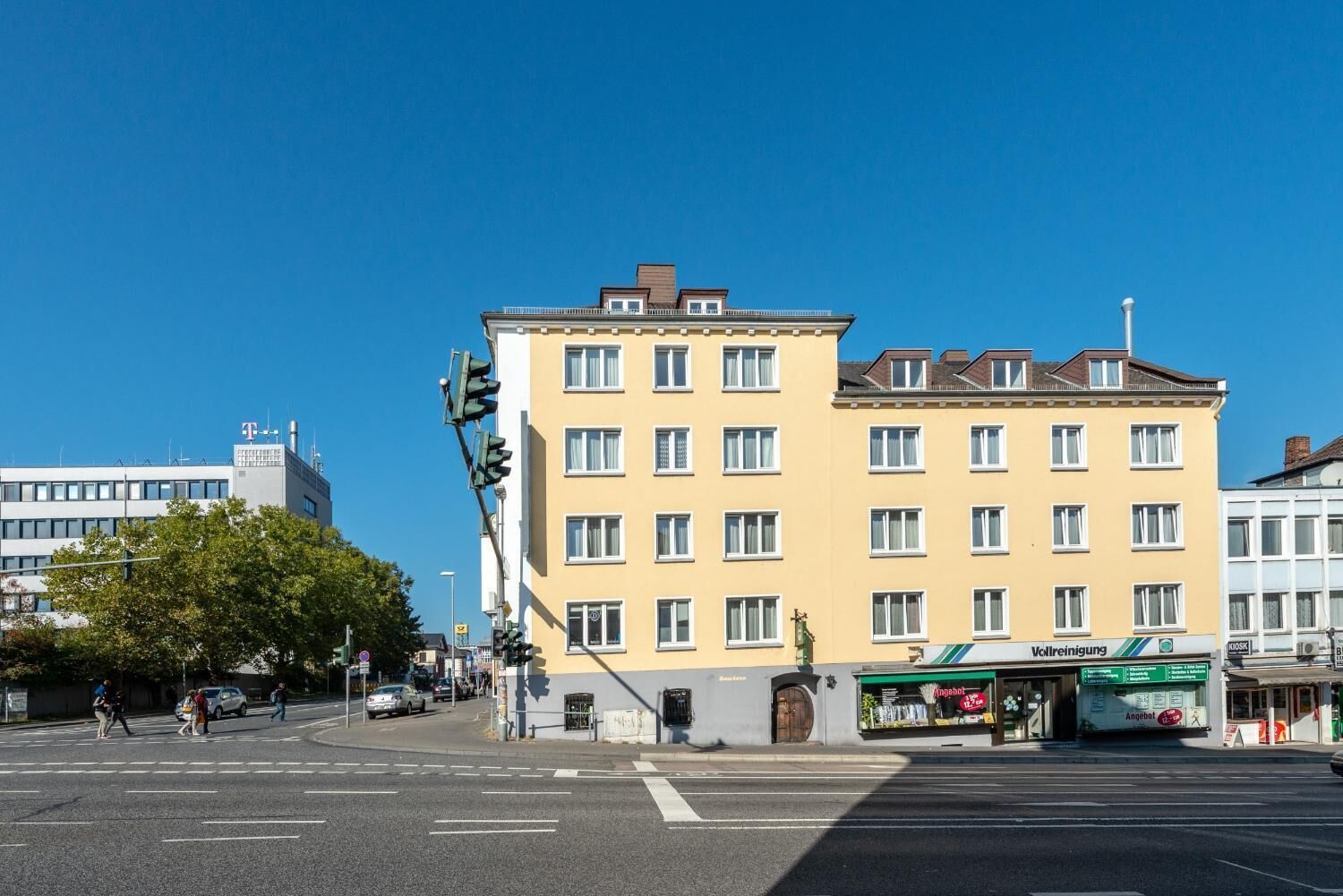 A multi-story building with a yellow facade, a visible storefront with signage, and a clear blue sky.