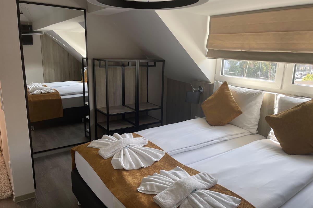 Une chambre d’hôtel avec un lit, un miroir, une fenêtre et un luminaire au plafond.