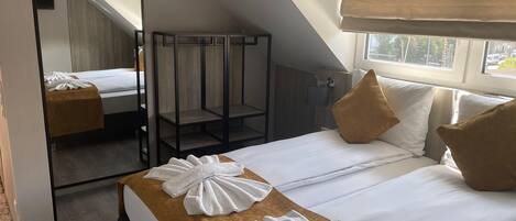A hotel room with a bed, a mirror, a window, and a ceiling light.