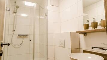 A bathroom with a glass-enclosed shower, a white sink, and a mirror above it.