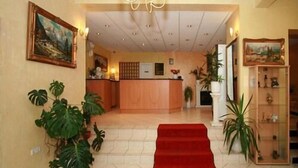 A hotel lobby with a reception desk, large potted plants, a red carpet, and artwork on the walls. - Liebig Hotel (Giessen)