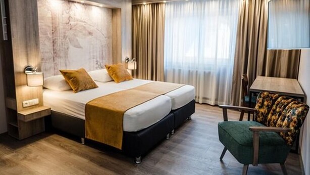 A modern hotel room with a large bed, a small table, a chair, and a large window with curtains. - Liebig Hotel (Giessen)