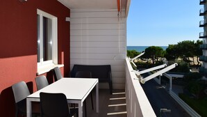 A balcony with a white table and chairs, overlooking a beach and buildings.