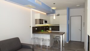 A modern kitchen with a built-in microwave, bar stools, and a dining area with a sofa.