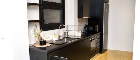 A modern kitchen with black cabinets, a stainless steel sink, and a coffee machine.