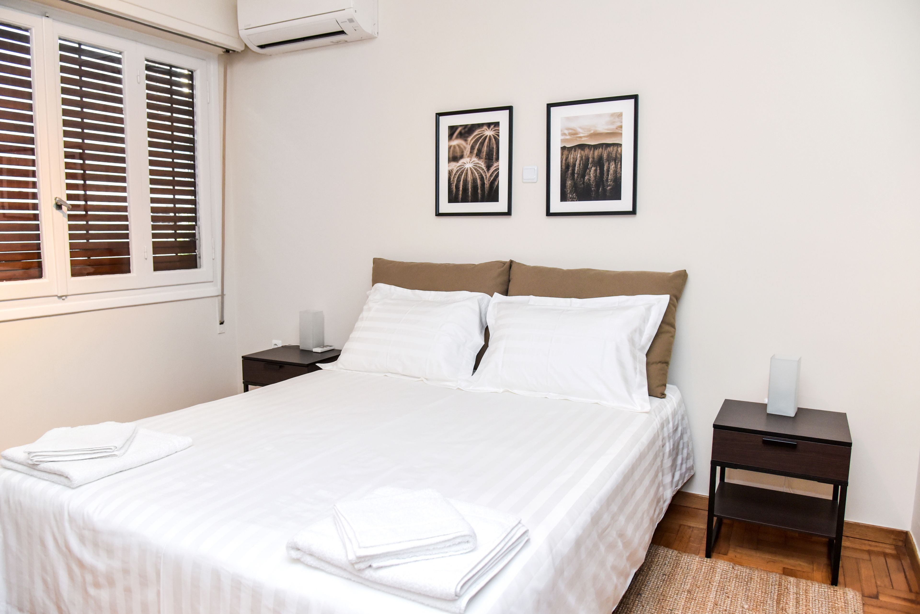 A neatly made bed with white linens and two pillows, a bedside table with a lamp, and two framed pictures on the wall.