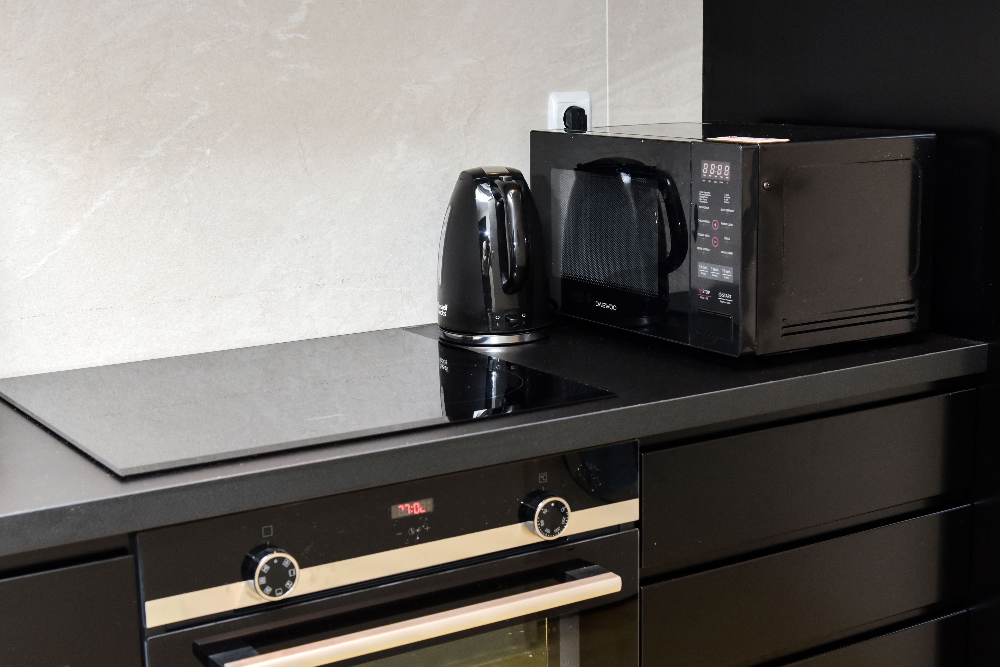 A kitchen with a black countertop, a coffee maker, a microwave, and a built-in oven.