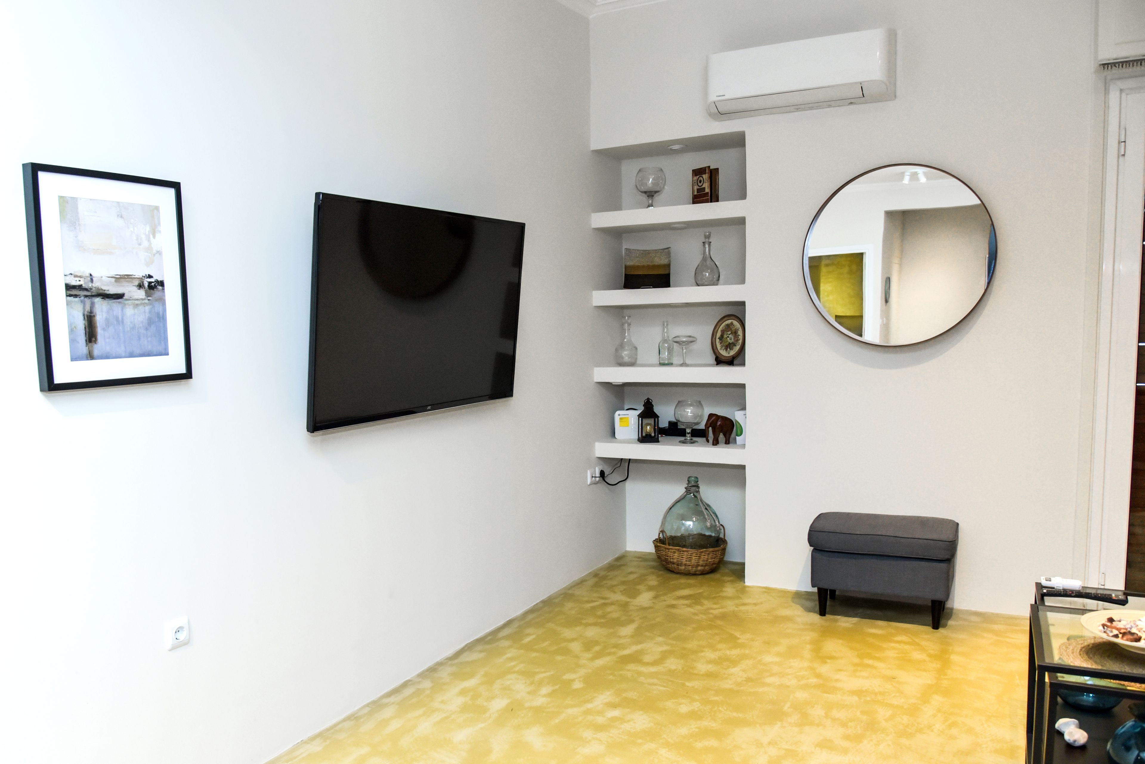 Un salon moderne avec un téléviseur à écran plat, un miroir rond et une étagère ornée d’objets décoratifs.