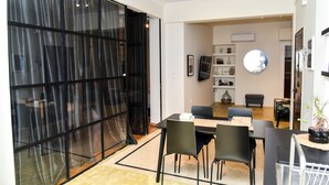 A dining area with a table set for four, surrounded by chairs, in a room with a large window and a wall-mounted mirror.