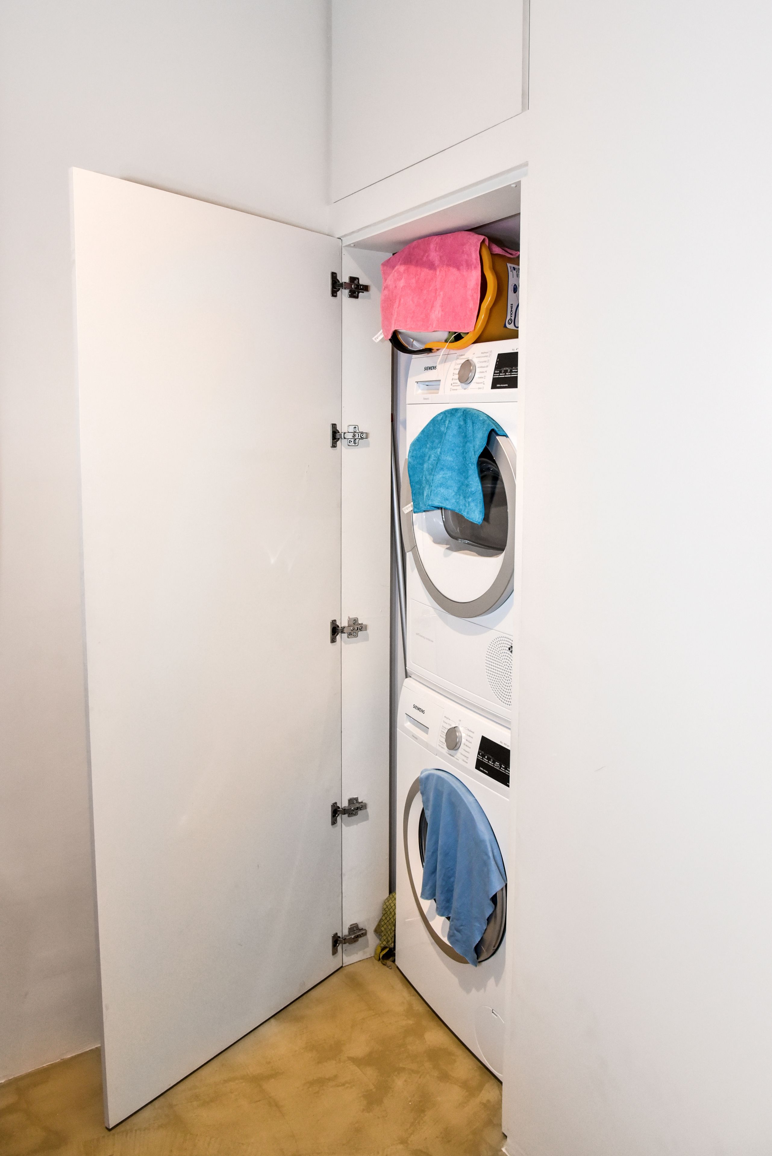 A laundry room with a white door, a stacked washer and dryer, and a blue towel hanging on the dryer.