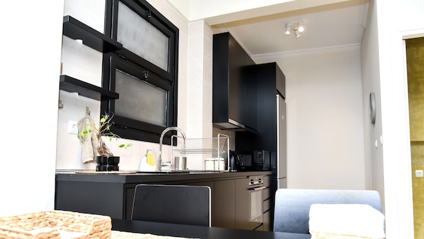 A modern kitchen with black cabinets, a microwave, and a sink. There is a dining area with a table and chairs.
