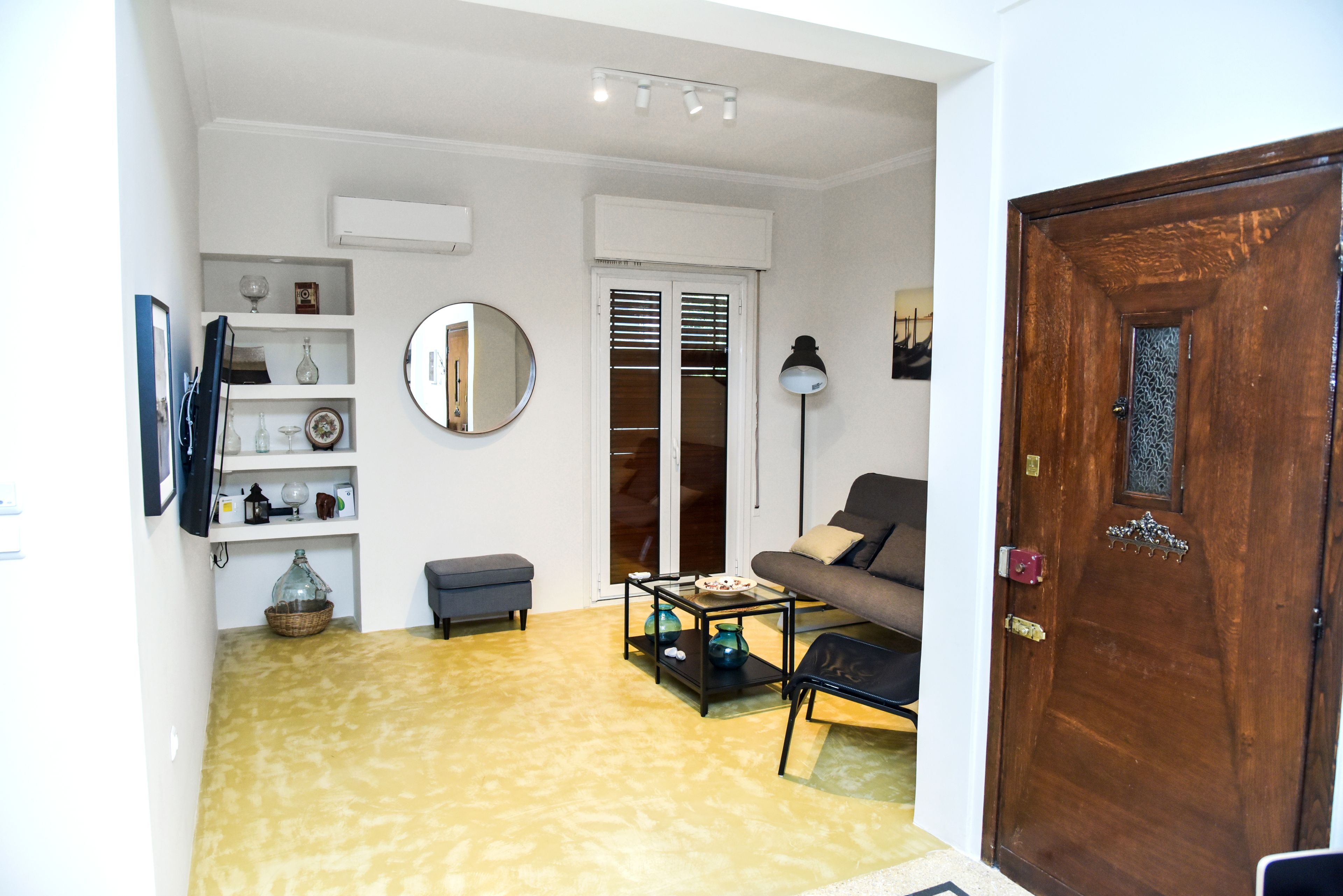 A living room with a sofa, coffee table, and a small side table. There is a wooden door and a mirror on the wall.