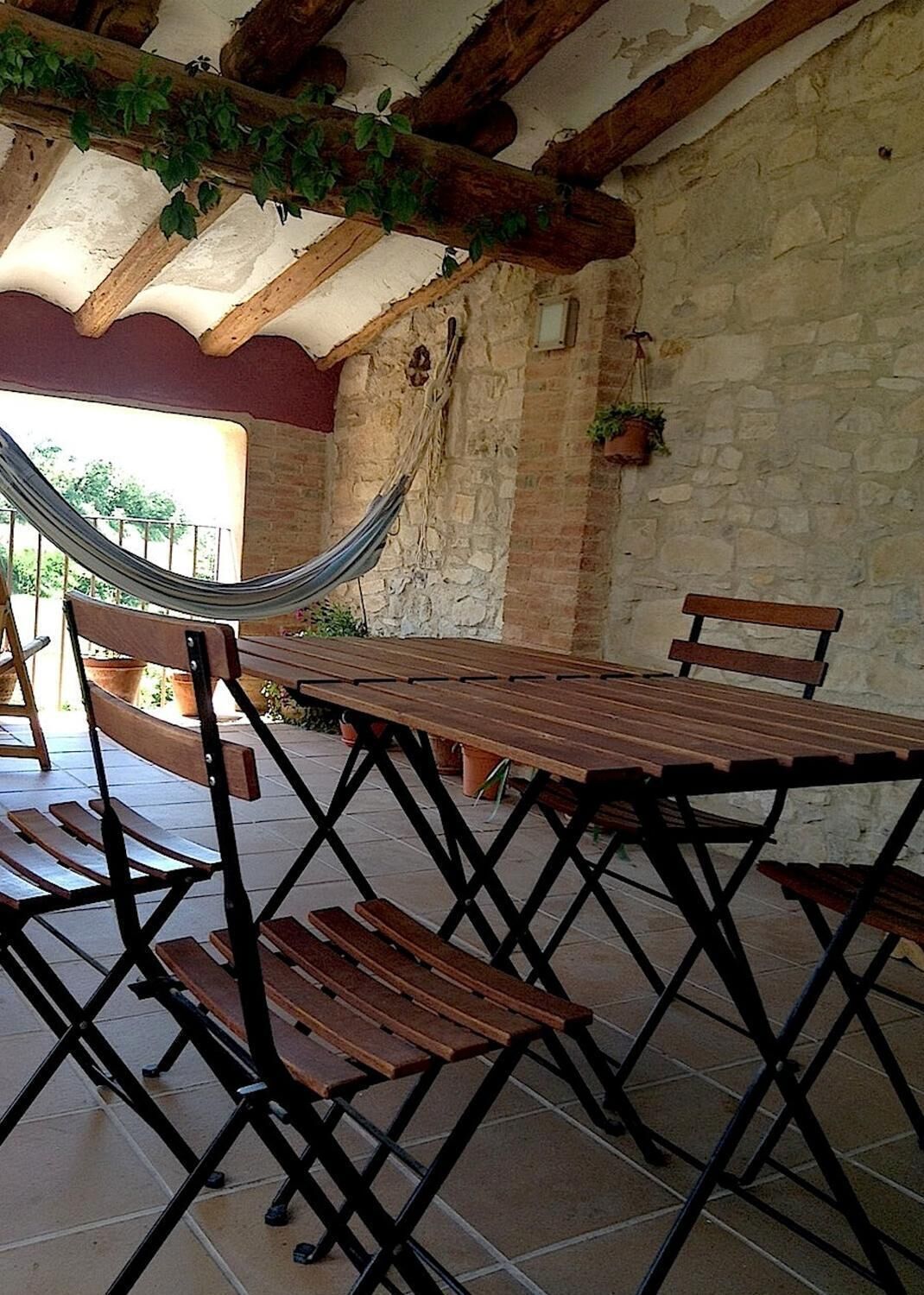 An outdoor patio with a wooden table and benches, a hammock, and stone walls.