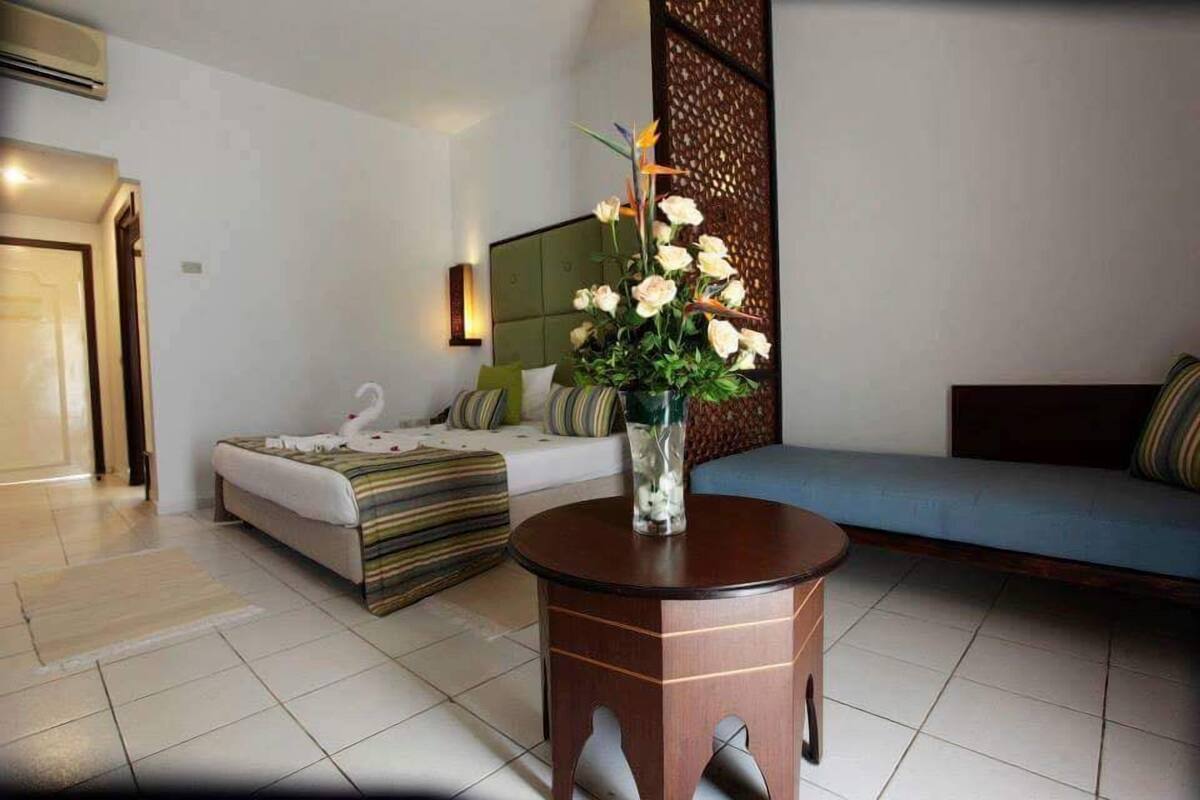 A hotel room with a bed, a sofa, a round wooden table, and a decorative vase with flowers.