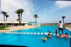 Un área de piscina con palmeras, sillas de descanso y sombrillas.