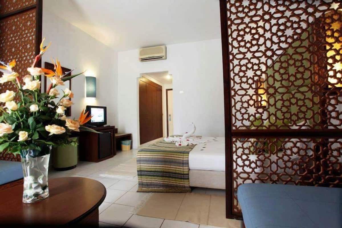 A hotel room with a bed, a bedside table, a chair, a decorative screen, and a vase with flowers.
