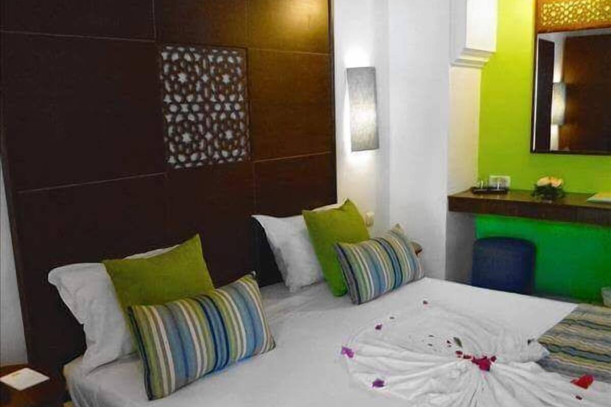 A hotel room with a large bed, a headboard with a patterned design, a bedside table, and a green accent wall.