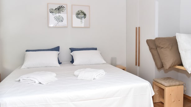 A neatly made bed with white linens and two pillows, a small wooden stool, and two framed wall art pieces. - Modern  Apartment at Exarchia 1 bed 2 pers  (Athens)