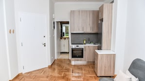A modern kitchen with wooden cabinets, a built-in oven, and a grey sofa in a living area. - Modern  Apartment at Exarchia 1 bed 2 pers  (Athens)
