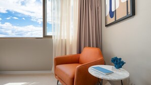 Una habitación moderna con un ventanal grande, un sillón naranja, una mesita redonda con un libro y un florero azul.