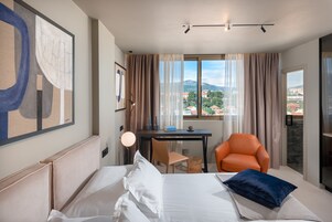 Une chambre d’hôtel avec un lit, un bureau, une chaise orange et une vue sur la ville.