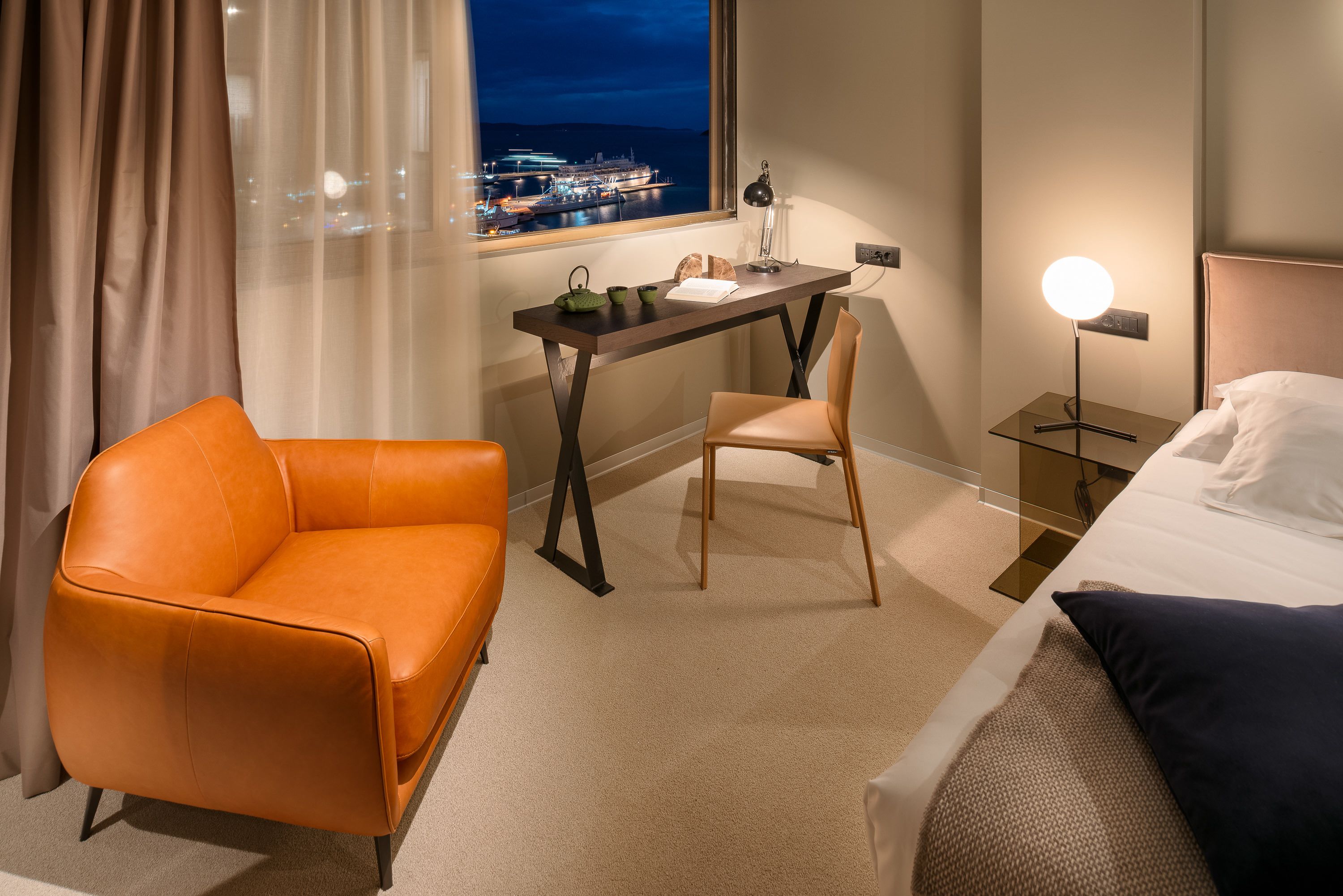 A hotel room with a desk, orange sofa, and a bed.