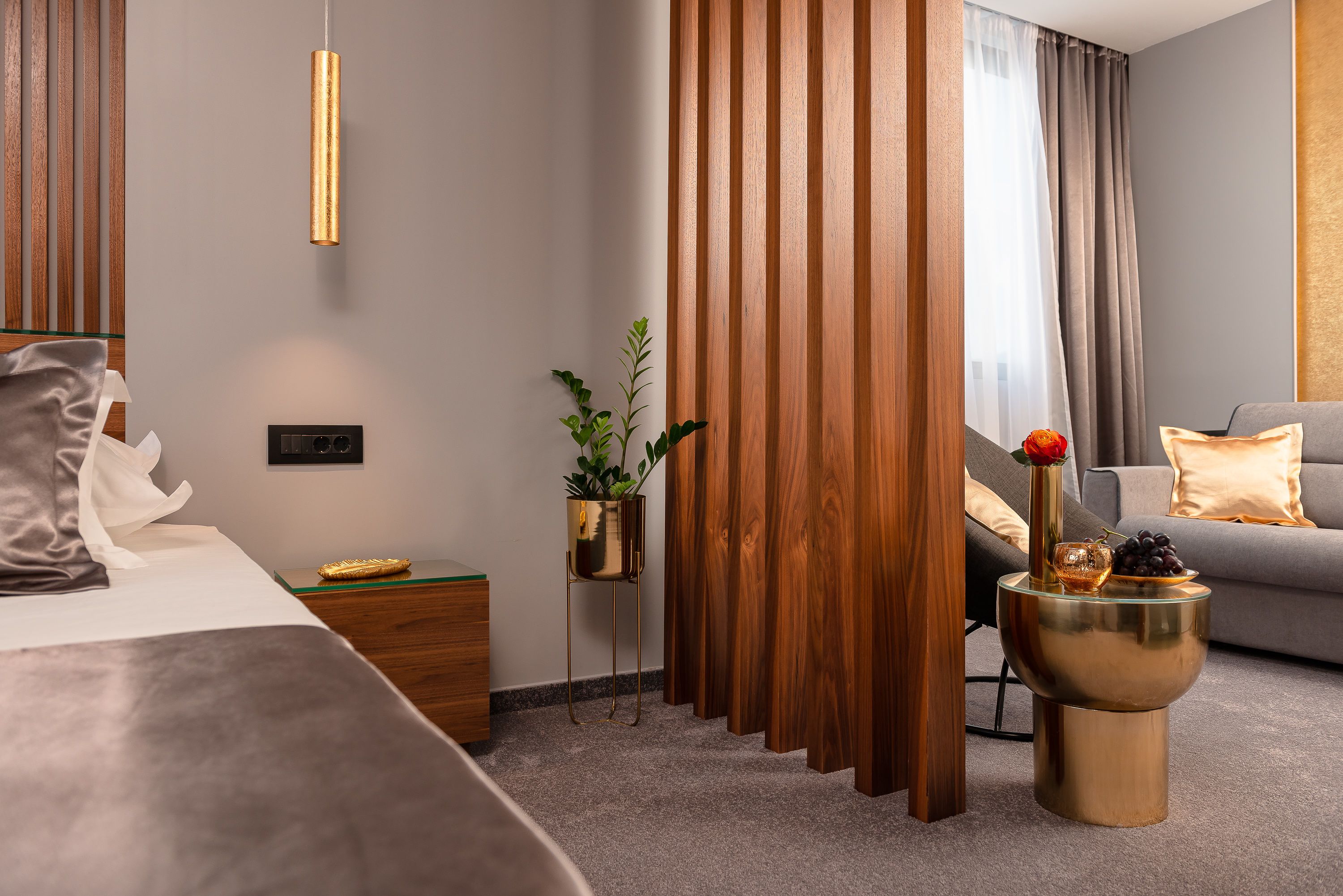 Una habitación de hotel moderna con una cama, una mesita de noche con lámpara, una planta pequeña, un cuenco decorativo y un sofá.