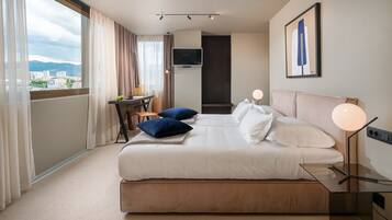 Quarto de hotel com uma cama grande, uma escrivaninha com cadeira, televisão e vista para a cidade.