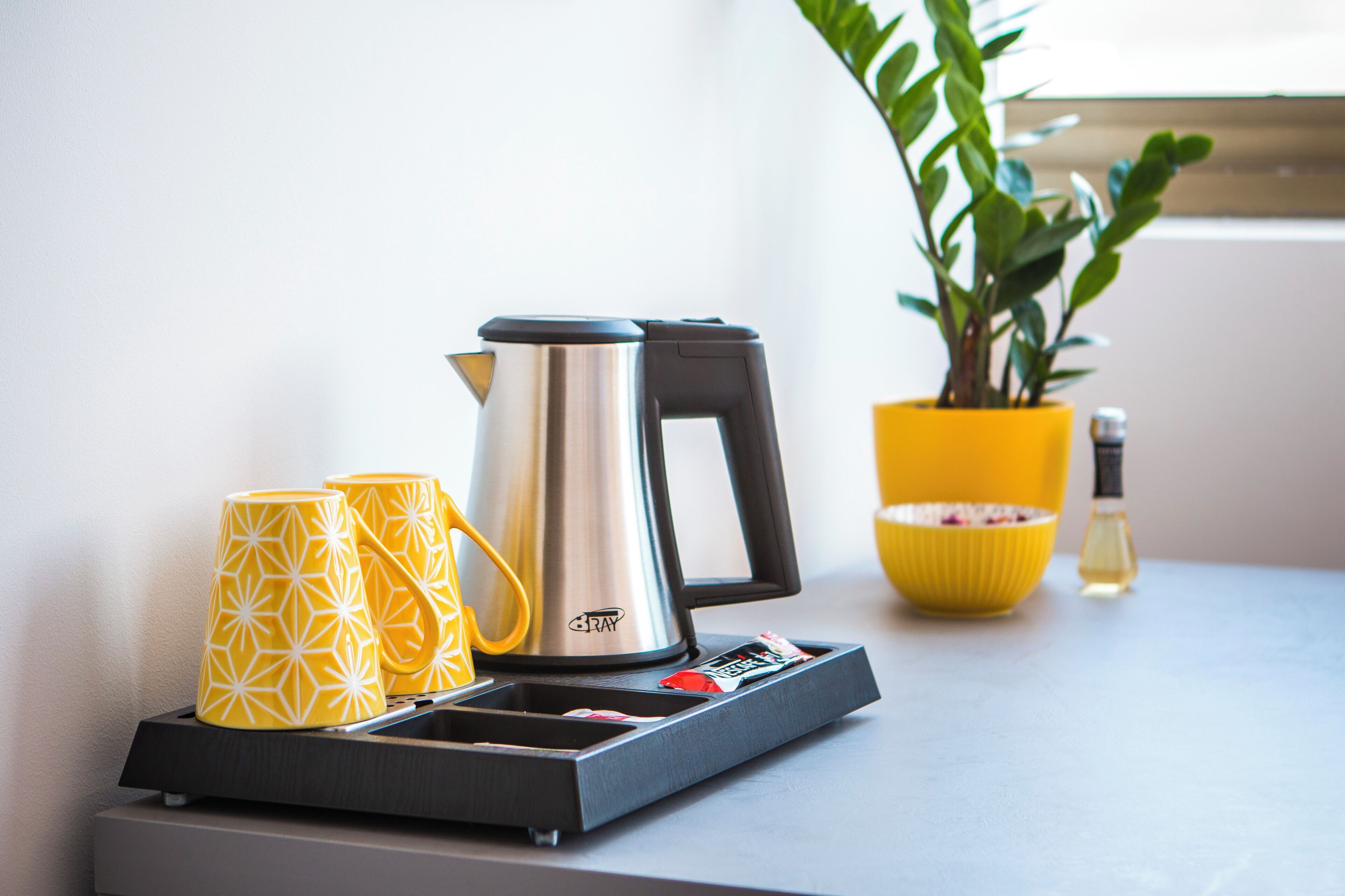Eine Küchenarbeitsplatte mit einer Kaffeemaschine, zwei gelben Tassen, einer gelben Schüssel und einer Topfpflanze.