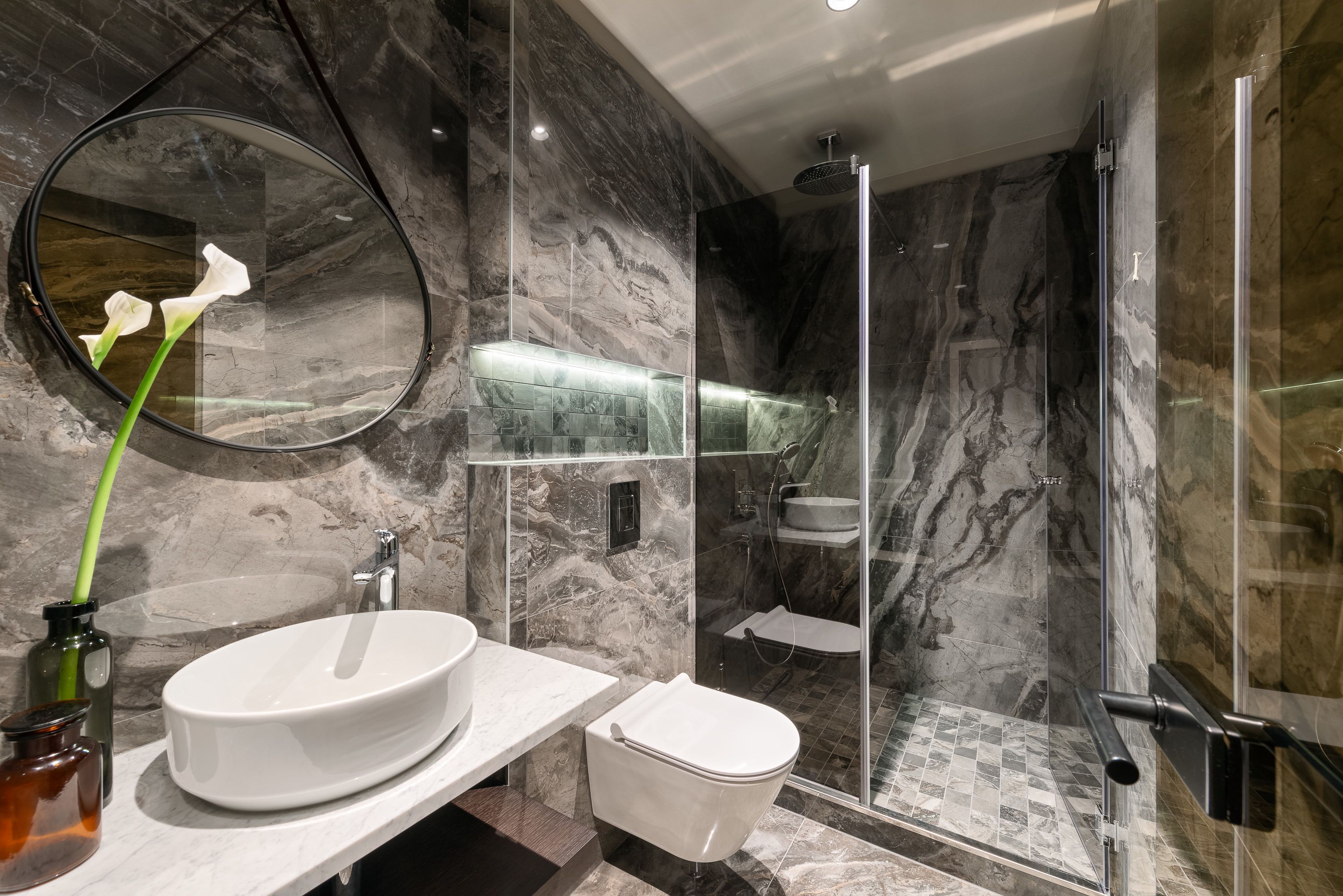 A modern bathroom with a marble sink, a toilet, a glass-enclosed shower, and a large mirror.